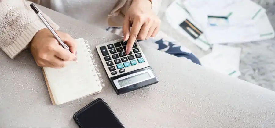 Mão de mulher a escrever com caneta em caderno e calculadora