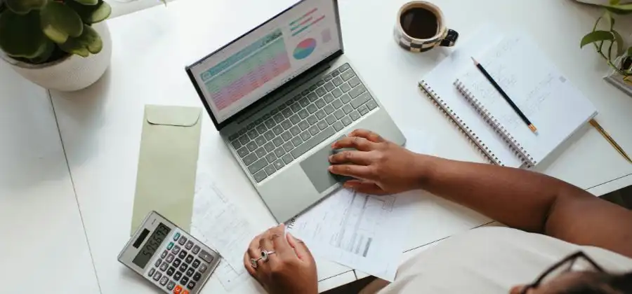 Mulher em secretária ao computador com estatísticas na tela e em folhas mais calculadora para simbolizar dados do salário médio baixo de Portugal