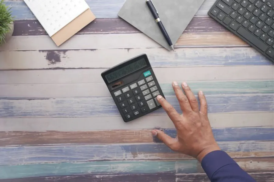 Calculadora em mesa de madeira às cores roxa e verde e mão esticada a carregar em tecla da calculadora