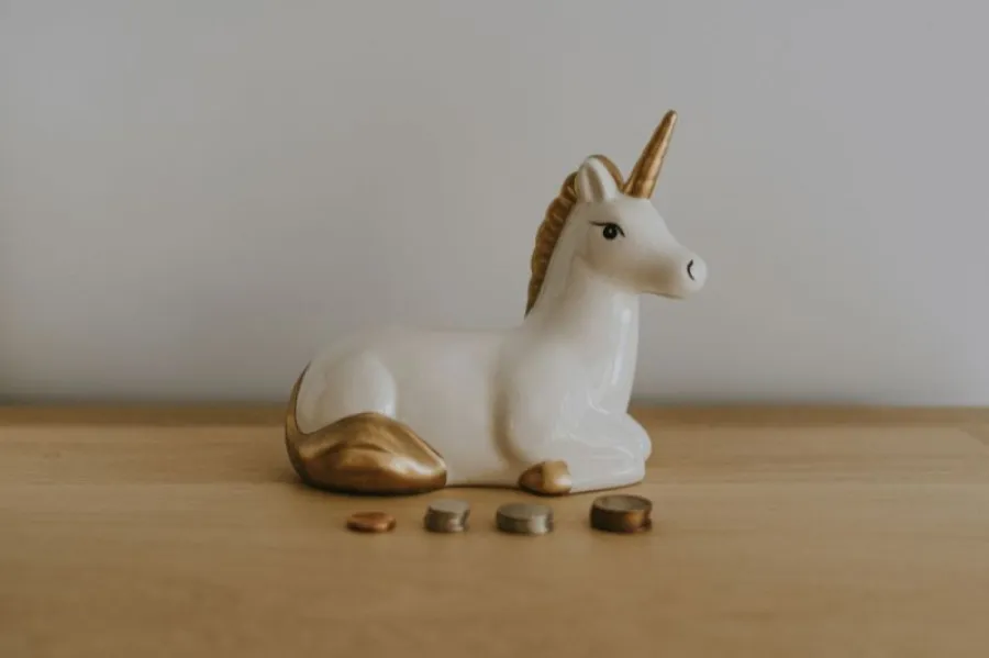 Unicórnio de mealheiro em branco e dourado com molhos de moedas à frente