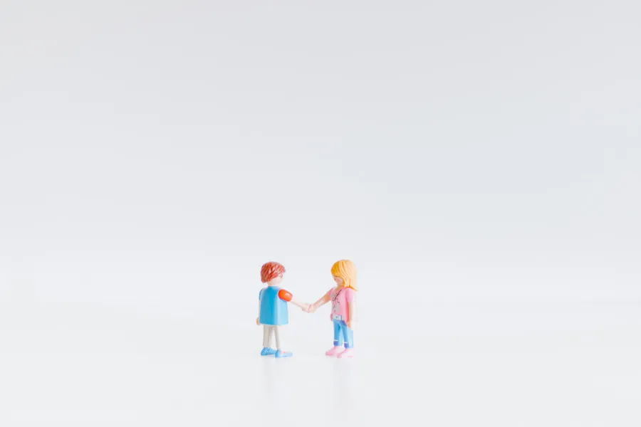 Miniaturas de um casal de mãos dadas, representando união de facto ou relação amorosa, sobre fundo branco minimalista.