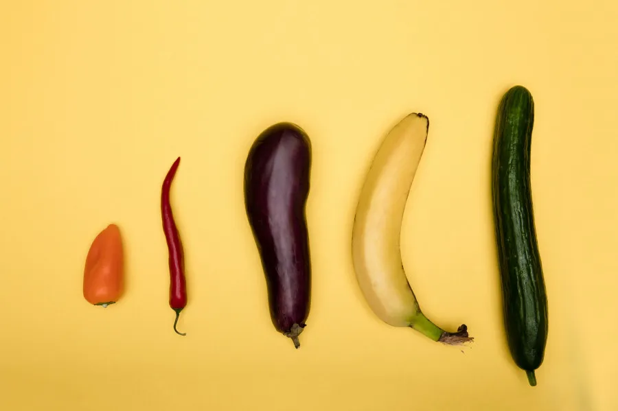 Vários legumes e frutas dispostos por ordem de tamanho sobre fundo amarelo, incluindo pimento, malagueta, beringela, banana e pepino.