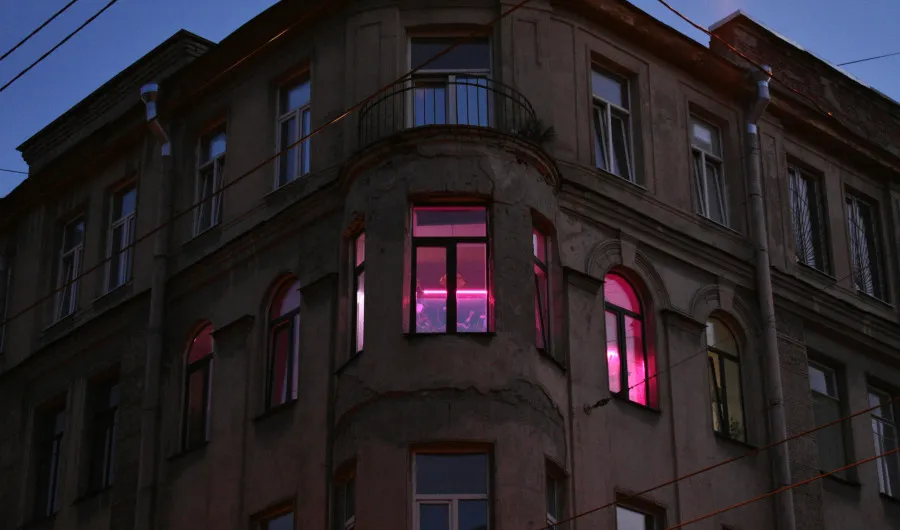 Fachada de prédio antigo ao anoitecer, com luzes cor-de-rosa acesas no interior de alguns apartamentos.