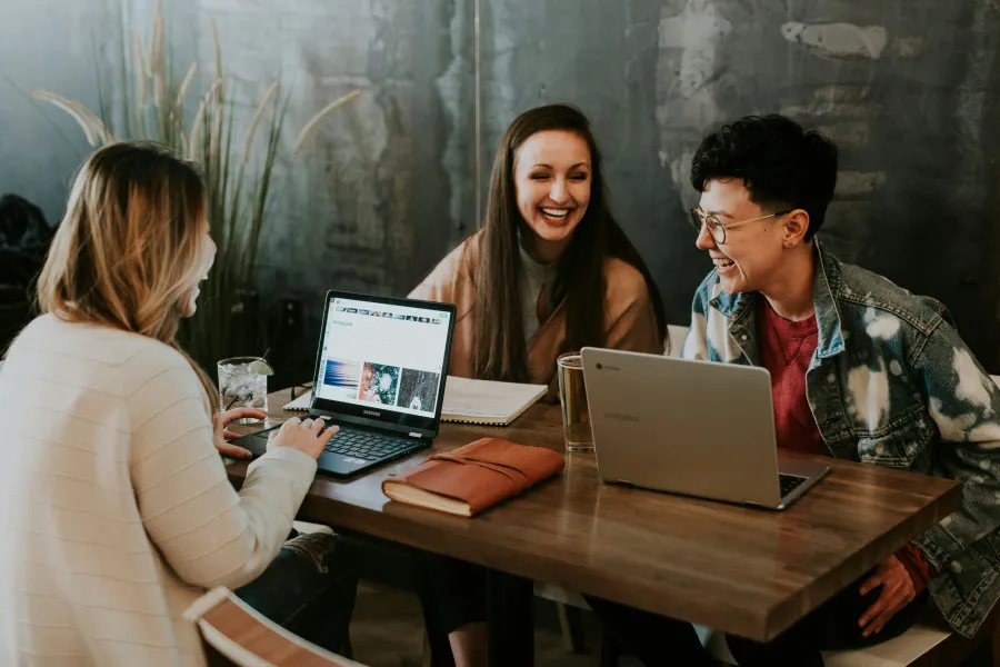 Três jovens sentados juntos numa sala, em volta de uma mesa, trabalhando diante do computador.