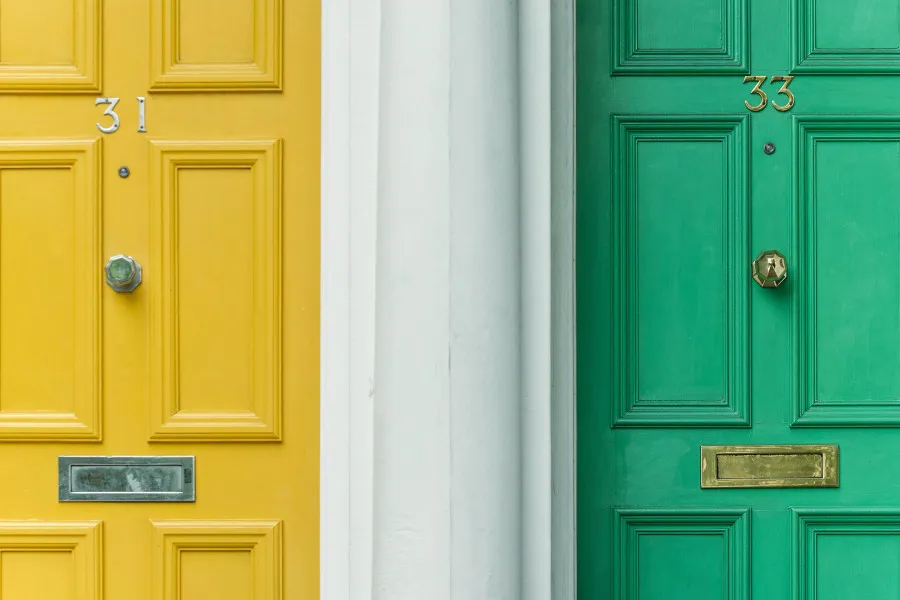 Duas portas lado a lado – uma amarela e outra verde – simbolizando duas casas. A imagem representa o conceito de contratar um segundo crédito habitação.