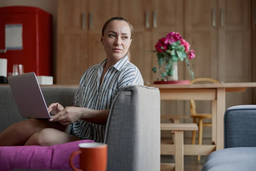 Mulher sentada no sofá, com computador no colo.