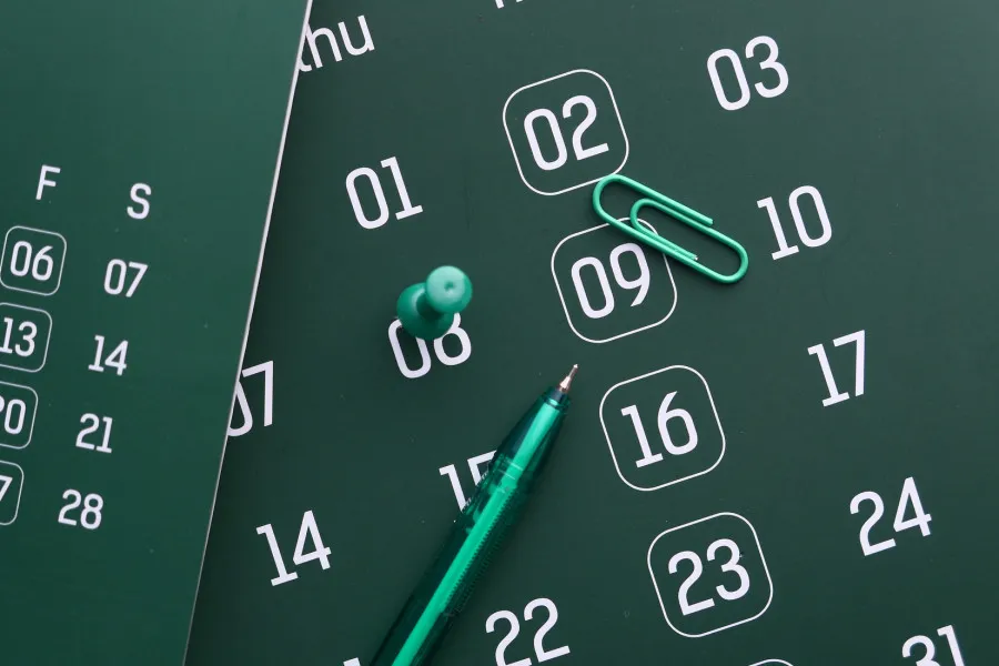 Calendário verde, com caneta e clipe da mesma cor.