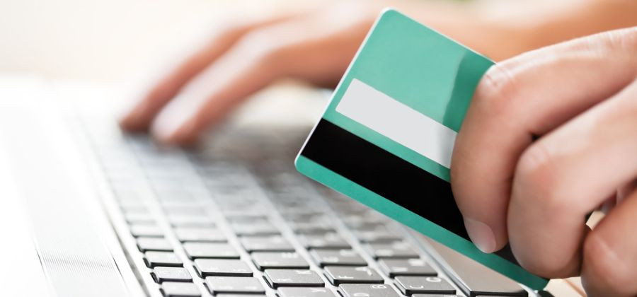 Teclado com mãos a segurar cartão bancário para compras online sustentáveis