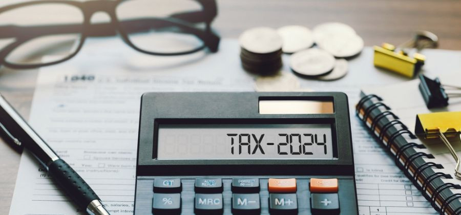 Calculadora com tax 2024, IMI, caneta, caderno, óculos, clips e moedas em cima de folhas sob mesa