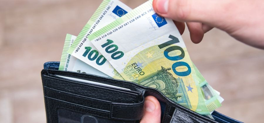 Carteira em mãos a retirar notas de 100 euros simbolizando prestação de maio