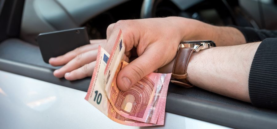 Mãos à janela de carro com notas de 10 euros para simbolizar pagamento de IUC