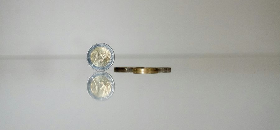 Moeda de dois euros em pé e moedas deitadas para simbolizar poupar dinheiro